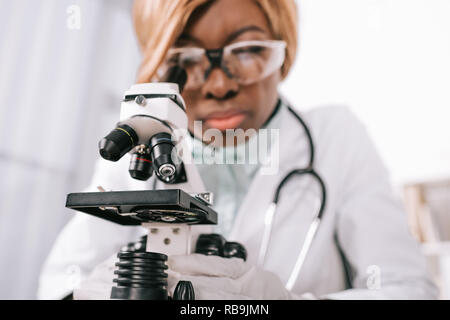 Messa a fuoco selettiva del microscopio con africani femmina scienziato americano sullo sfondo Foto Stock