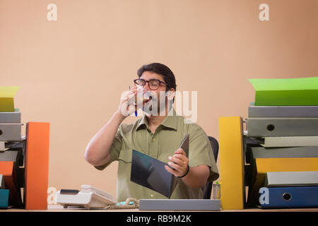 Imprenditore studiando i file mentre si sorseggia un bicchiere di tè seduto alla sua scrivania in ufficio. Foto Stock