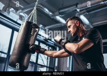 Basso angolo vista del bel boxer training con sacco da boxe in palestra Foto Stock