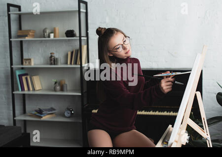 Bella ragazza in Borgogna maglione seduto e pittura su tela a casa Foto Stock