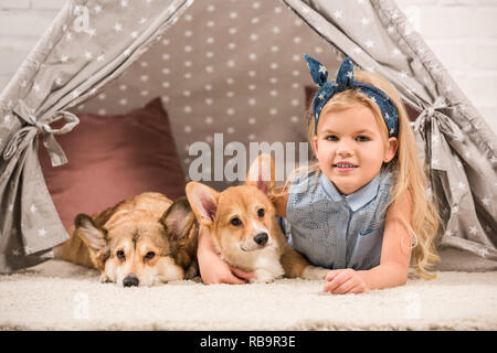 Carino bambino con welsh corgi cani giacente in wigwam e guardando la fotocamera Foto Stock