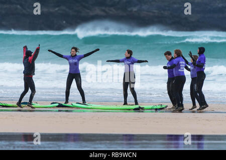 I surfisti principianti il riscaldamento con il loro maestro fino all'inizio di una lezione di surf a Fistral Beach in Newquay Cornwall. Foto Stock
