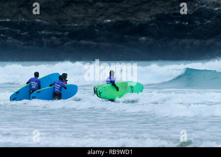 I surfisti principianti che trasportano le loro tavole da surf e passeggiate in mare per una lezione di surf a Fistral Beach in Newquay Cornwall. Foto Stock