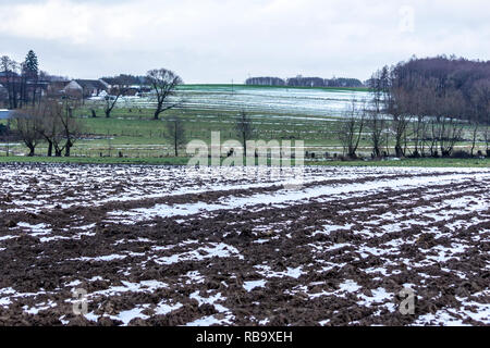 Piccole strisce di neve sui campi arati e prati. Forest e caseificio in background. L'inizio dell'inverno in Europa. Foto Stock