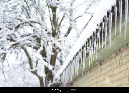 Ghiaccioli sul tetto della casa con neve e sfondo sfocato. Bellissimo paesaggio invernale. Ghiaccioli house. Foto Stock