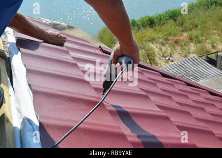 Copritetti contraente installazione tetto metallico e piastrelle con il cacciavite. Tetto metallico e l'installazione. Foto Stock