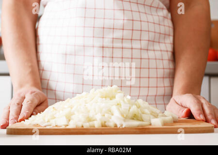 Una donna di cuochi in cucina, su una tavola di legno si trova un mucchio di cipolla tritata. Un sano cibo fresco. Close-up Foto Stock