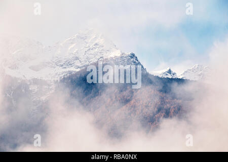 Montagne coperte di neve sulla parte superiore. Vista attraverso le nuvole. Chiavenna, Italia Foto Stock