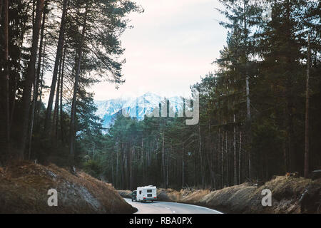 Strada mistico nella foresta con camper auto a cavallo su di esso. Le montagne sullo sfondo. Innsbruck, Austria Foto Stock