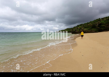Giovane donna in giacca gialla in piedi, camminare in acque poco profonde su una bellissima spiaggia appartata, Ishigaki, Giappone Foto Stock