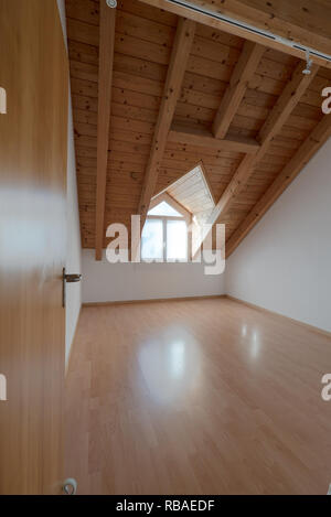 Svuotare spaziosa e luminosa stanza in un appartamento ristrutturato con pavimento in parquet e pareti bianche e inclinata di soffitto in legno con un abbaino Foto Stock