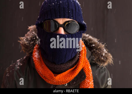 Ritratto di un singolo maschio avventuriero invernali indossando un caldo manto verde con cappa di pelliccia, un blu berretto da sci, un foulard arancione e nero in stile retrò gli occhiali di protezione Foto Stock