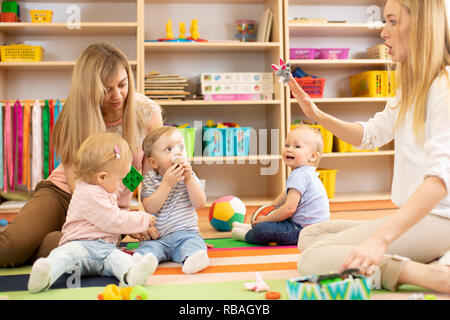 Gruppo di bambini in vivaio. Insegnante di materna assistente e giocare con i bambini sul tappeto accogliente Foto Stock