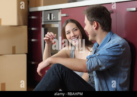 Felice inquilini che mostra nuove chiavi di casa seduti sul pavimento della cucina Foto Stock