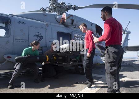 Stati Uniti I marinai, assegnato all'elicottero Maritime Strike Squadron (HSM) 71, caricare un modulo AGM-114 Hellfire missile su un MH-60R Sea Hawk mentre Ordnanceman aviazione di seconda classe Alberto Gomez, a destra dalla città di Sioux, Iowa, sovrintende a bordo guidato-missile destroyer USS Spruance (DDG 111) nel Mare Arabico, 21 dicembre 2018. Spruance è distribuito negli Stati Uniti Quinta Flotta area di operazioni a sostegno di operazioni navali per garantire stabilità marittimo e la sicurezza nella regione centrale di collegamento del Mediterraneo e del Pacifico attraverso l'Oceano Indiano occidentale e tre strategici punti di strozzatura. Foto Stock