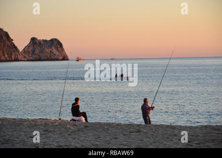 Alanya, Turchia, 29 ottobre 2018: I pescatori pescano lungo la spiaggia di Cleopatra durante un tramonto dorato, con il cielo bagnato dalle calde sfumature serali. Foto Stock