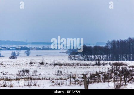 La coperta di neve i campi e prati. Villaggio e delle aziende lattiere in background. L'inizio dell'inverno in Europa. Foto Stock