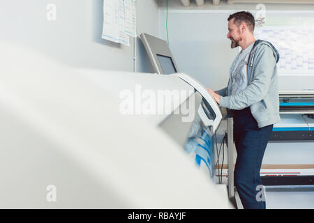 Uomo al lavoro su stampante di grande formato in agenzia di pubblicità Foto Stock