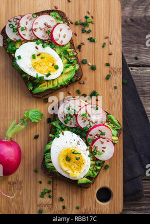 Toast con avocado, uova, ravanello cipolla verde e semi di lino in legno rustico sfondo. Vista dall'alto. Foto Stock