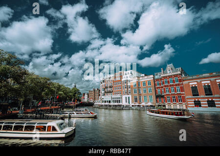 Classico paesaggio urbano di Amsterdam. Barche di crociera galleggiante sul canale, il river side promenade, caffetterie, tipica architettura olandese. Scena urbana e white fl Foto Stock