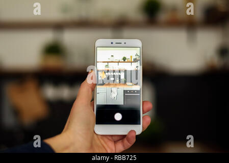 Tenendo cucina foto dal telefono cellulare. Aprire il piano bianco da cucina in legno con ripiani aperti Foto Stock