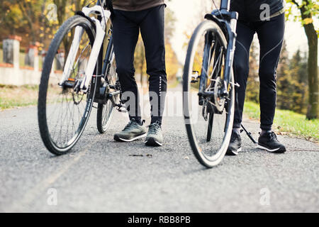 Gambe e piedi di coppia con electrobikes all'aperto su una strada nel parco. Foto Stock