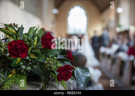 Garofani rossi in bouquet in chiesa un giorno di nozze con la sposa e lo sposo in soft focus in background sul loro giorno di nozze Foto Stock