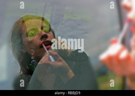 La bionda signora mettendo sul rossetto e utilizzando la finestra auto come lo specchio Foto Stock