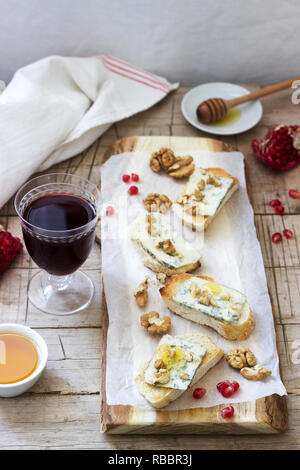 Panini con formaggio blu, melograno, miele e noci servita con vino rosso. Stile rustico. Foto Stock