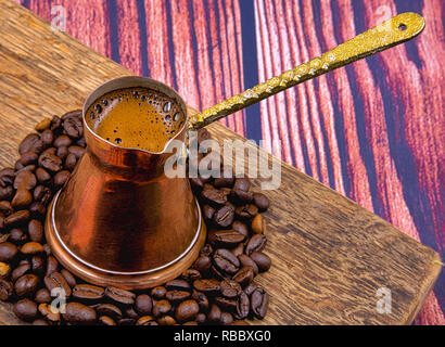 Forte colore nero caffè servito in un vecchio rame crogiolo su una vecchia tavola di legno, i chicchi di caffè intorno a. Chiudere, orizzontale piana, vista in pianta da sopra Foto Stock