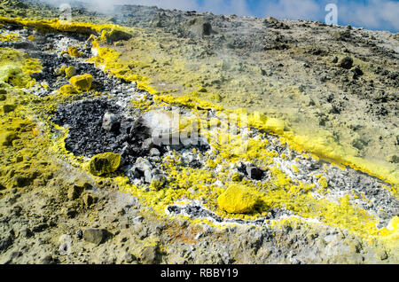 Giallo zolfo cristalli sulle rocce di superficie del cratere di un vulcano sull'isola di Vulcano arcipelago delle Eolie, in Sicilia. Gas, vapore e fumo da fumarola Foto Stock
