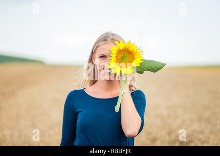 Donna sorridente girasole tenendo in mano nel campo. Foto Stock