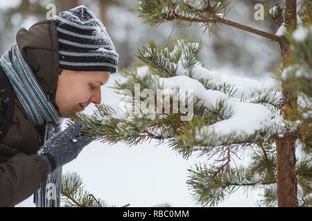 Giovane uomo lo sniffing di un ramo di pino in inverno foresta. Concetto di res, aromaterapia, uno stile di vita sano, in armonia con la natura. Foto Stock