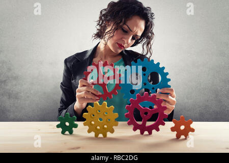 Imprenditrice tenta di collegare pezzi di ingranaggi. Concetto di lavoro di squadra, partnership e integrazione Foto Stock
