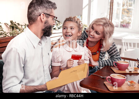 Gioiosa eccitato ragazza seduta con i suoi genitori Foto Stock