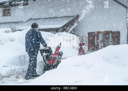 Un uomo che pulisce la neve da marciapiedi con spalaneve in Baviera Germania Bad Toelz Miesbach Foto Stock