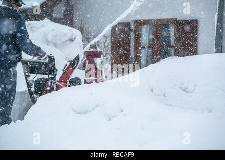 Un uomo che pulisce la neve da marciapiedi con spalaneve in Baviera Germania Bad Toelz Miesbach Foto Stock