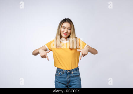 Bella giovane donna asiatica punto verso il basso per lo spazio in bianco su sfondo grigio. Foto Stock