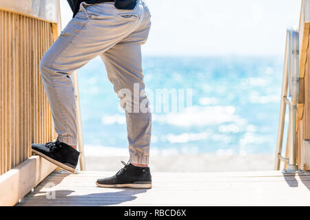 Hollywood, Stati Uniti d'America Beach Boardwalk in Florida Miami con gradini in legno Scale e uomo gambe generico con bokeh sfocato sfondo sfocato di blu oceano wat Foto Stock