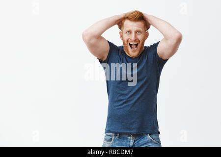 L'uomo urla di rammarico e shock. Studio shot di bello maturare redhead guy nella disperazione, toccando i capelli, urlando e fissando scioccata e devestated in telecamera, sensazione di delusione oltre il muro grigio Foto Stock