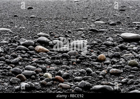 Primo piano della grande nero pietre vulcaniche o granelli di sabbia sulla spiaggia di Reynisfjara, Islanda con Riva e lucenti rocce umide Foto Stock