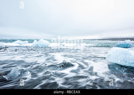 Vista del paesaggio del ghiacciaio blu Iceberg in laguna Jokulsaron lago spiaggia di diamante in Islanda con sabbia nera e una lunga esposizione delle onde di acqua Foto Stock