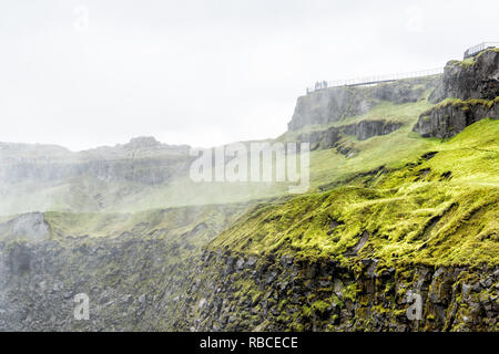 Islanda Dettifoss cascata elevato angolo si affacciano vista di nebulizzazione di acqua e la scogliera rocciosa con persone di turisti nel lontano lontano da erba verde Foto Stock