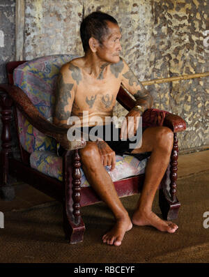 Anziani Iban uomo con tatuaggi Tribal seduto nella sedia in area comunale del Longhouse Mengkak, Batang Ai, Sarawak (Borneo), Malaysia Foto Stock