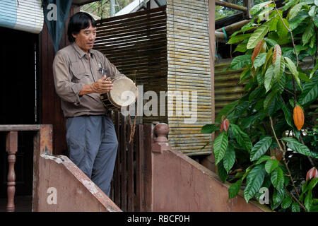 Uomo Bidayuh suonare il tamburo sul portico di casa, Kampung Annah Rais, Sarawak (Borneo), Malaysia Foto Stock