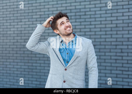 Ritratto di quizzical considerato bello uomo barbuto in stile casual in piedi di toccare la sua testa, di pensare e di provare a trovare la vera risposta. piscina studio Foto Stock