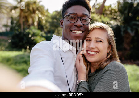 Bella interracial giovane facendo una selfie all'esterno. L'uomo africano con donna caucasica prendendo un autoritratto. Foto Stock