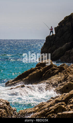 Un coraggioso pescatore pesca in mare con una canna da pesca in piedi sul pericoloso alte scogliere con l'oceano sotto Foto Stock