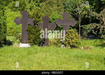 Tre grandi croci con alberi e cespugli in un cimitero Foto Stock