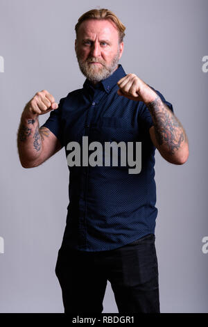 Studio shot maturo di uomo barbuto con la mano i tatuaggi getting leggere Foto Stock